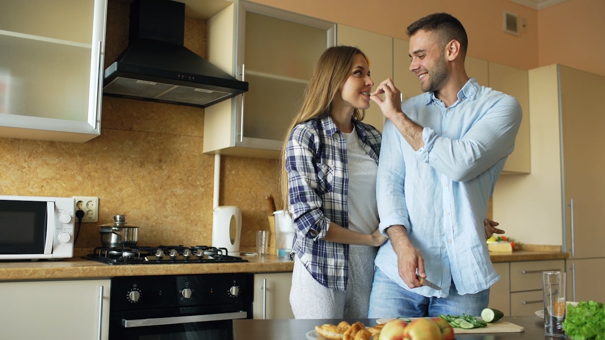 Happy young couple in the kitchen. Handsome man meet and feed his girlfriend early morning at home